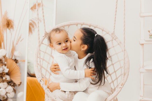 Um menino e uma menina estão sentados em uma cadeira de vime pendurada e rolando. as crianças se amam e se abraçam.