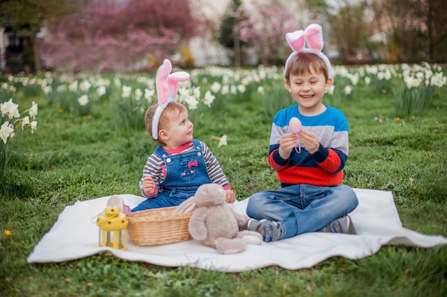 Um menino e uma menina fofos estão sentados na grama perto dos narcisos