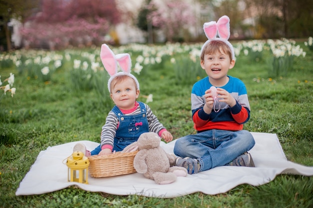 Um menino e uma menina fofos estão sentados na grama perto dos narcisos