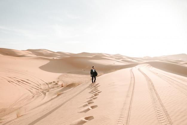 Um menino em seu terno de casamento andando nas dunas do deserto com o nascer do sol no fundo