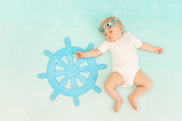 Um menino em um fundo azul dorme com o volante de um navio e óculos de natação