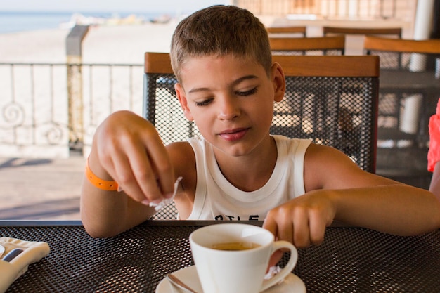 Um menino em um restaurante no terraço com uma xícara