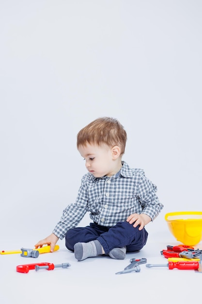 Um menino em uma camisa com um capacete e uma ferramenta de brinquedo Fundo branco Ferramenta de construção de brinquedos para crianças