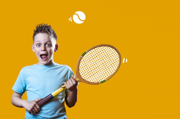 Um menino em uma camiseta leve com uma raquete de tênis e uma bola na laranja