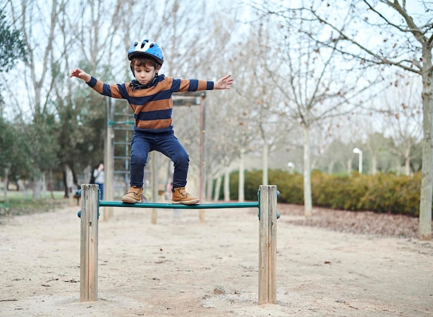 Um menino encantador em um capacete brinca no parque escalando e pulando obstáculos