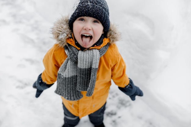 Um menino encantador pega flocos de neve com a língua num belo parque de inverno laranja.