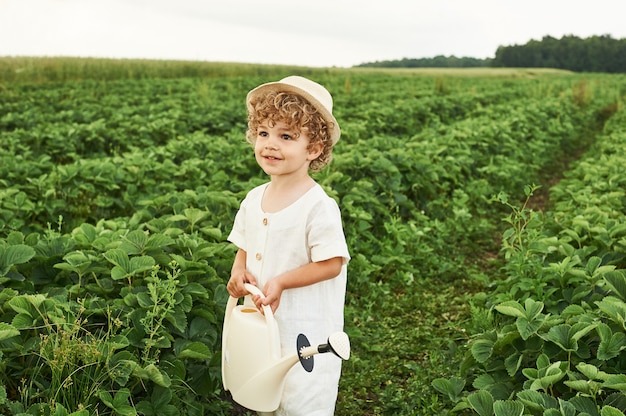 Um menino encaracolado em um chapéu branco e roupas de linho no campo