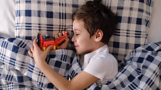 Um menino engraçado e alegre deita-se na cama e abraça o seu brinquedo favorito.