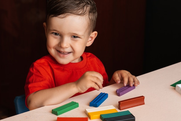 Um menino esculpe figuras de plasticina multicolorida sentado a uma mesa. Educação pré-escolar. Passatempo. Auto desenvolvimento