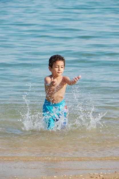 Um menino espirra na água em uma praia.