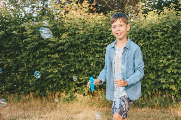 Um menino está brincando com bolhas de sabão em um parque de verão entre a vegetação