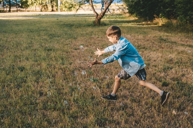 Um menino está brincando com bolhas de sabão em um parque de verão entre a vegetação