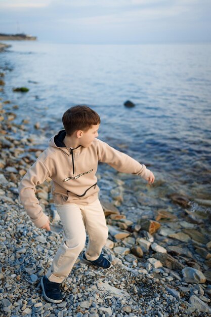 Um menino está em uma praia rochosa em frente a um lago.