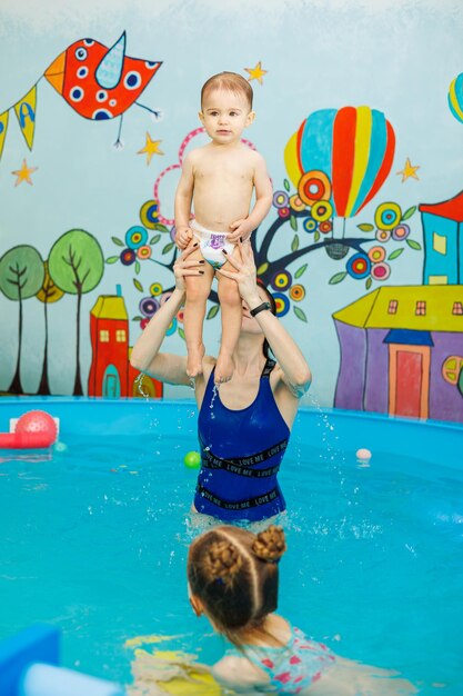 Um menino está nadando na piscina com um treinador ensinando crianças a nadar na escola de natação infantil