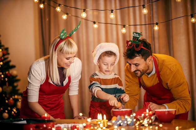 Foto um menino está quebrando o ovo e fazendo biscoitos de pão de gengibre enquanto os pais o ajudam no natal