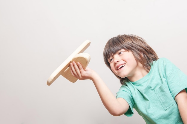 Um menino está segurando um brinquedo de avião de madeira e sorrindo