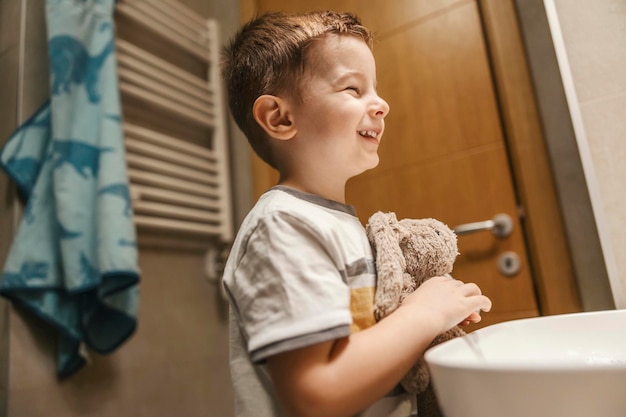 Um menino está sorrindo para o espelho enquanto está no banheiro com seu coelhinho pela manhã