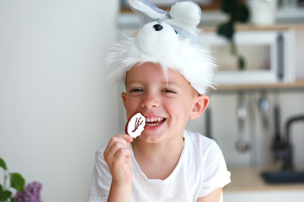 Foto um menino fantasiado de coelho come biscoitos de páscoa na forma de um ovo e ri feliz