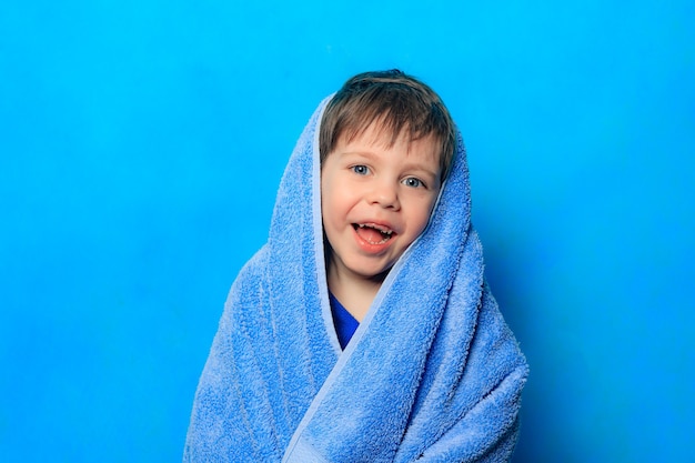 Um menino feliz com uma toalha sobre a cabeça em fundo azul