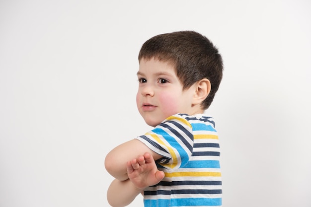 Um menino feliz de 4 anos em uma camiseta listrada segura as mãos perto do peito e olha de lado um lugar para texto