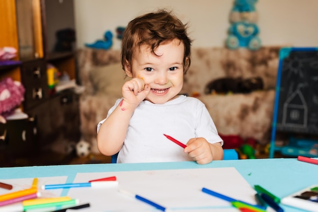 Um menino feliz desenha com marcadores coloridos em um pedaço de papel