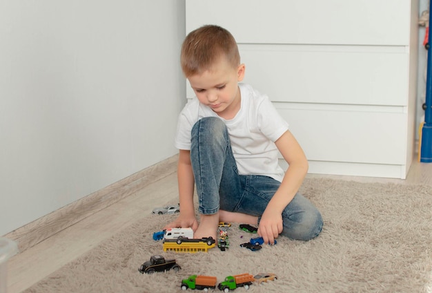 Um menino feliz e contente está brincando com muitos brinquedos favoritos no chão da casa os carros são seu brinquedo favorito o conceito de infância