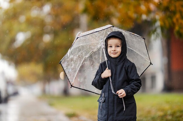 Foto um menino feliz está parado na rua com seu guarda-chuva no dia chuvoso