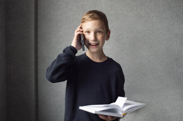 Um menino feliz está segurando um livro nas mãos e falando ao telefone