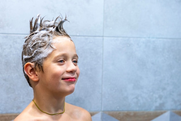 Um menino feliz lava a cabeça no banheiro com shampoo
