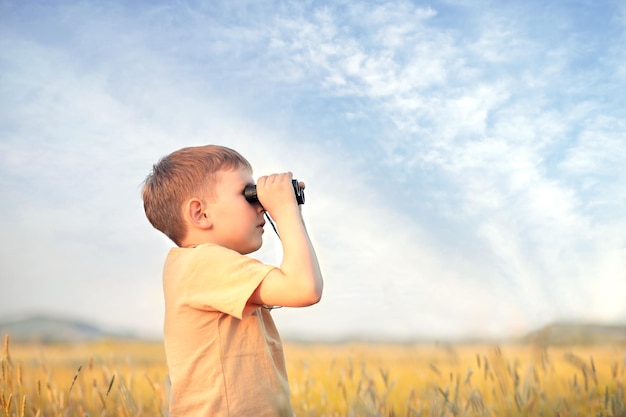 um menino fica em um campo e olha através de binóculos