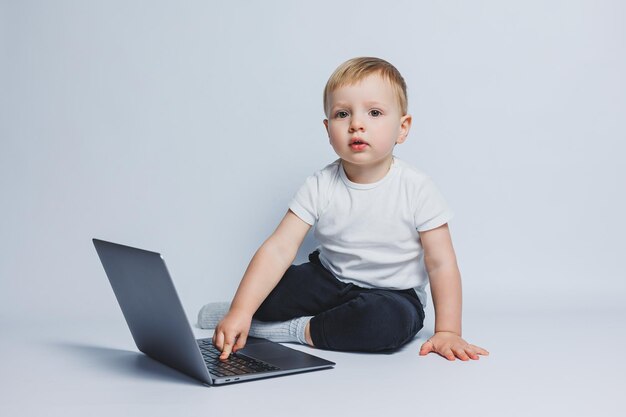 Um menino inteligente de 34 anos senta-se com um laptop em um fundo branco Uma criança em uma camiseta branca e calça preta se senta em um laptop e olha para a câmera Crianças modernas