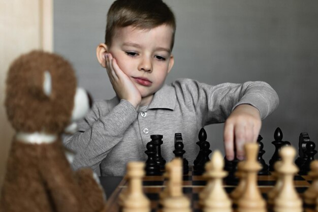 Um menino jogando xadrez com um ursinho de pelúcia