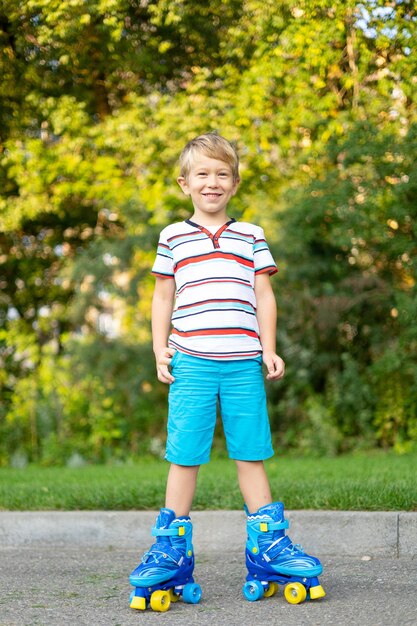 Um menino loiro bonitinho de patins está parado na grama sorrindo olhando para a câmera o conceito de jogos esportivos ao ar livre jogos ativos