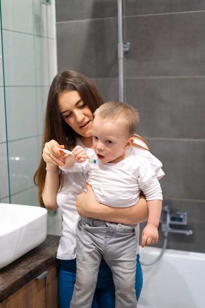 Um menino loiro e sua mãe estão brincando na banheira O bebê está escovando os dentes da mãe