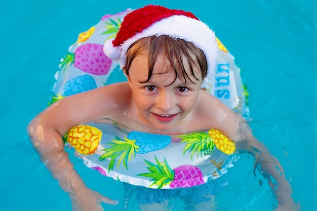 Um menino loiro feliz com um chapéu de Papai Noel e um menino de vida nadam na piscina