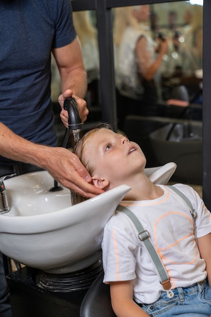 Um menino loiro lava o cabelo em uma barbearia antes de cortar o cabelo