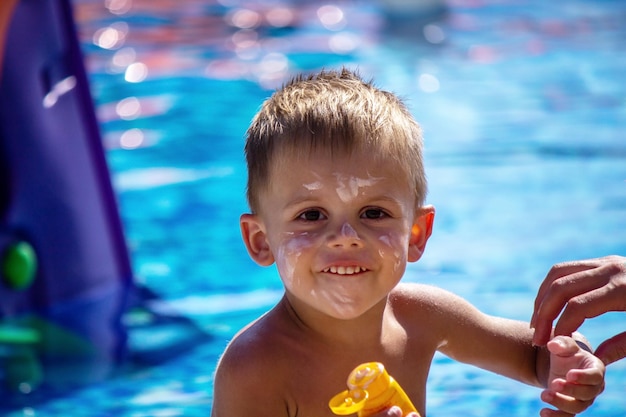 Um menino na piscina manchado com creme bronzeador Foco seletivo