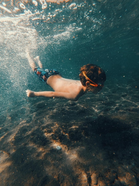 Um menino nadando debaixo d'água com a palavra mar no fundo