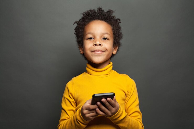 Um menino negro feliz e sorridente com um smartphone.