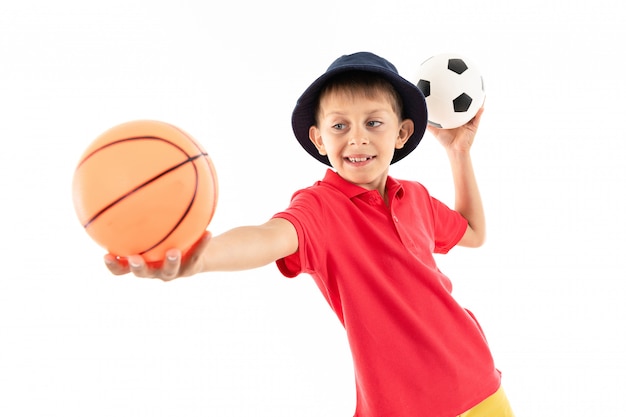 Um menino no Panamá, camisa amarela, shorts vermelho e tênis branco fica com bolas de basquete e futebol