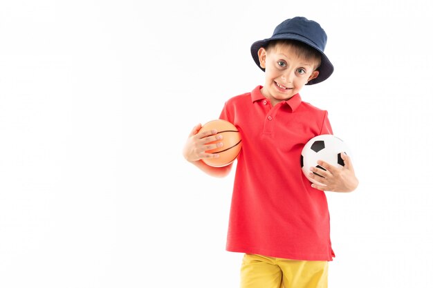 Um menino no Panamá, camisa amarela, shorts vermelho e tênis branco fica com bolas de basquete e futebol