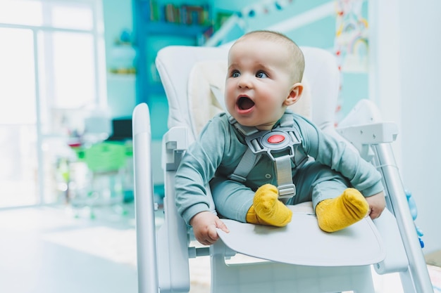 Um menino pequeno e bonito está sentado em uma cadeira alta para alimentar Cadeira de cozinha infantil para comer móveis infantis