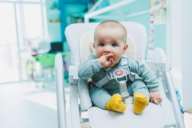 Um menino pequeno e bonito está sentado em uma cadeira alta para alimentar Cadeira de cozinha infantil para comer móveis infantis