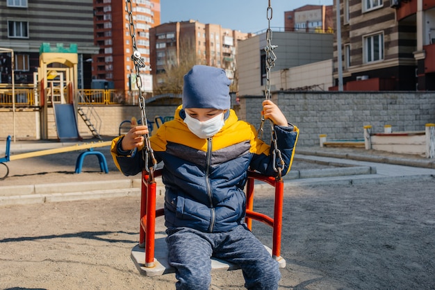 Um menino pequeno em uma máscara caminha no recreio durante a quarentena. Ficar em casa.