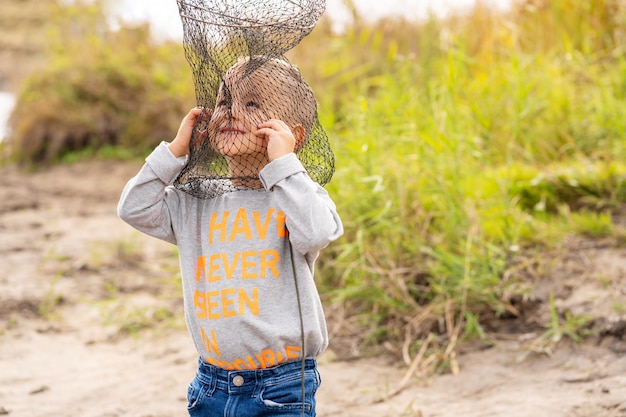 Um menino pescando e quer pegar o maior peixe. Menino bonitinho bagunçado na rede de peixe. Conceito de férias de verão.