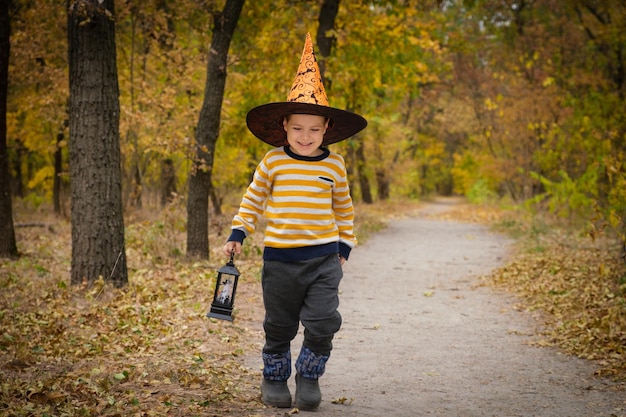 Um menino pré-escolar caminha com uma lanterna na floresta de outono de halloween