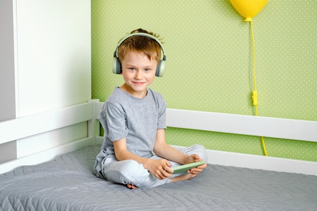 Um menino pré-escolar em fones de ouvido sem fio e usando telefone celular Crianças e conceito de tecnologia