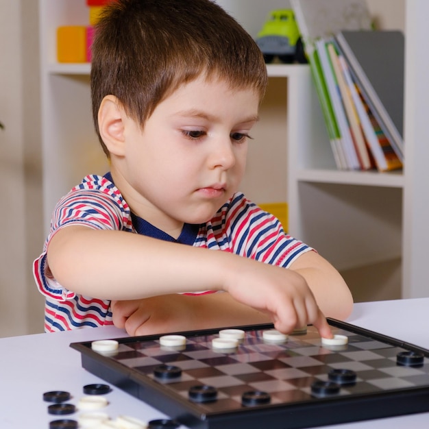 Um menino pré-escolar joga um jogo de tabuleiro de damas