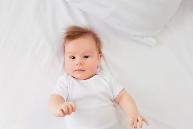 Um menino recém-nascido está descansando na cama, deitado de costas na cama. Infantil.