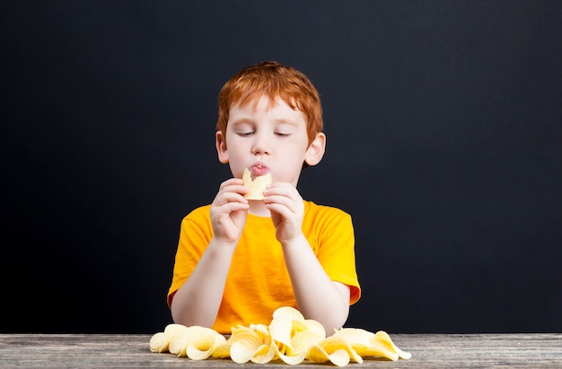 Um menino ruivo come e coleta deliciosas batatas fritas crocantes enquanto come